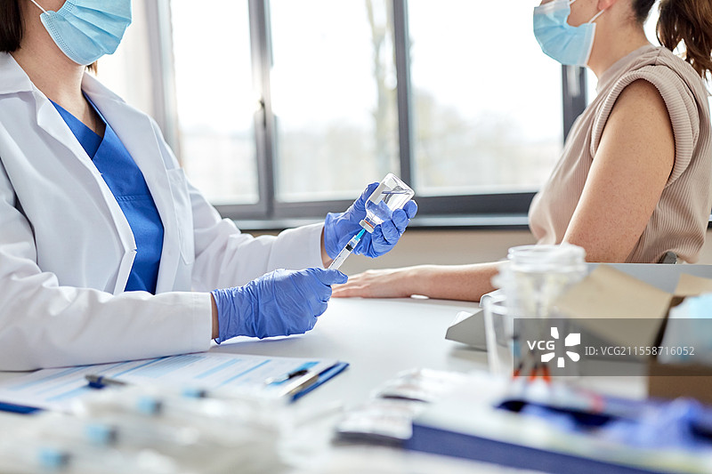 健康、医学和疫情概念 - 女性医生或护士佩戴防护口罩，使用注射器为患者接种疫苗。女性医生用注射器为患者接种疫苗。图片素材