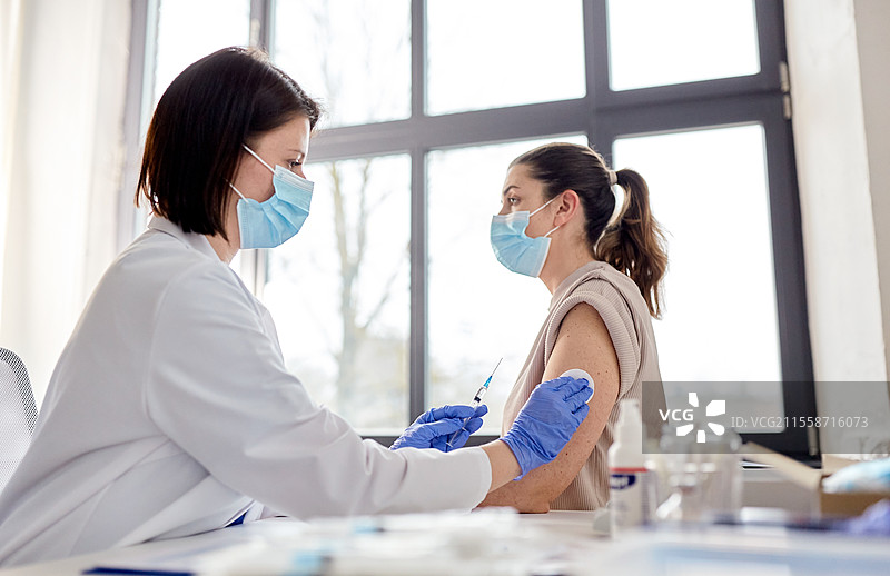健康、医学和疫情概念 - 女性医生或护士佩戴防护口罩，使用注射器为患者接种疫苗。女性医生用注射器为患者接种疫苗。图片素材