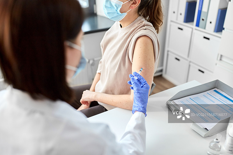 健康、医学和疫情概念 - 女医生或护士戴着防护手套，使用注射器为患者接种疫苗的特写。女医生用注射器为患者接种疫苗。图片素材