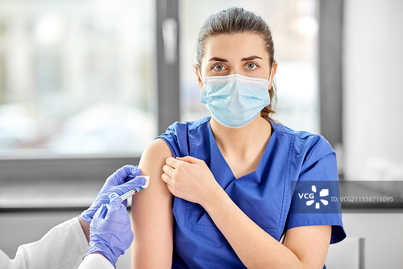 医疗、医学和疫情概念 - 女性医生或护士佩戴防护口罩，使用注射器为医务工作者接种疫苗。医生用注射器为医务工作者接种疫苗。图片素材