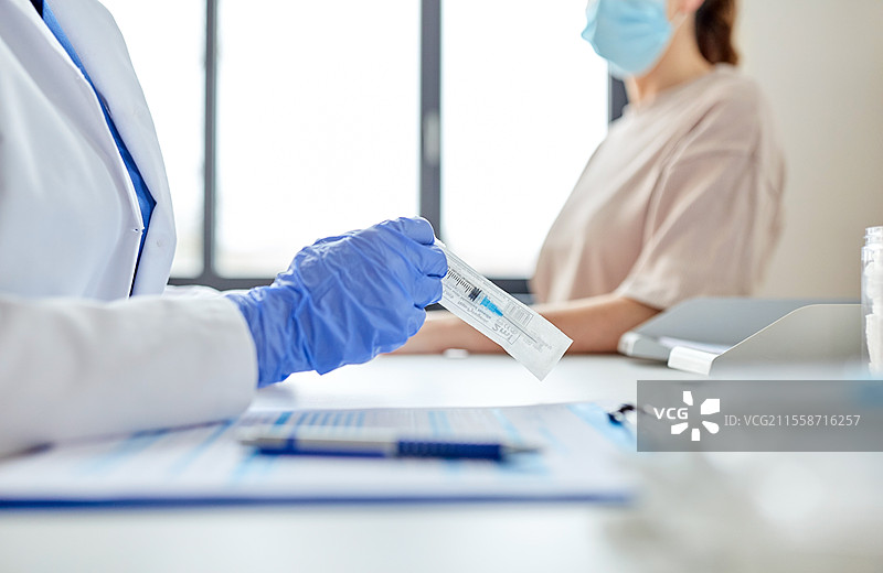 健康、医学和疫情概念 - 女性医生或护士佩戴防护口罩，正在打开疫苗注射器的包装，准备为医院的患者接种。女性医生手持注射器与患者在医院。图片素材