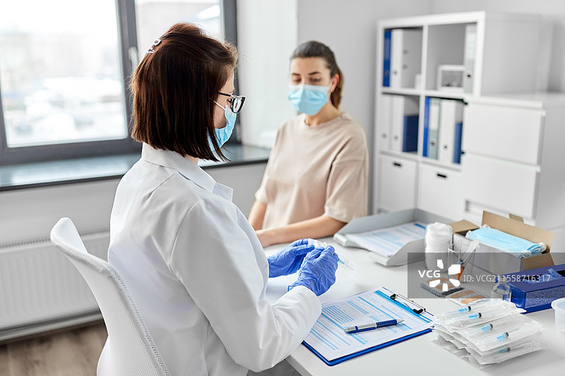 健康、医学和疫情概念 - 女性医生或护士佩戴防护口罩和手套，正在打开装有疫苗注射器的包装，准备为医院的患者接种。女性医生手持注射器与患者在医院。图片素材