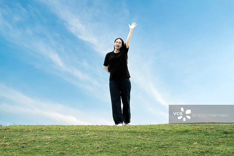 一个在晴朗蓝天下享受自由的年轻女子图片素材