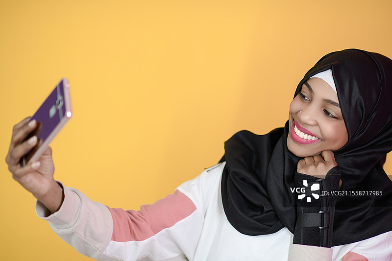 一位面带美丽微笑的非洲穆斯林女性在黄色背景下用手机自拍图片素材