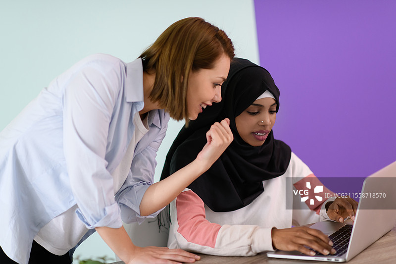 一位戴着头巾的非洲穆斯林女性微笑着坐在她的家庭办公室里，使用笔记本电脑参加在线会议。图片素材