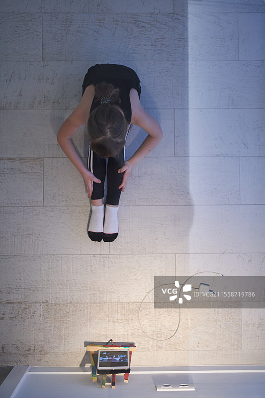 小女孩在家中观看平板电脑进行在线培训，同时进行健身和现代芭蕾舞练习。现代芭蕾舞学校的在线教育概念课程。在疫情隔离期间保持社交距离，自我隔离的居家时光。俯视图。图片素材