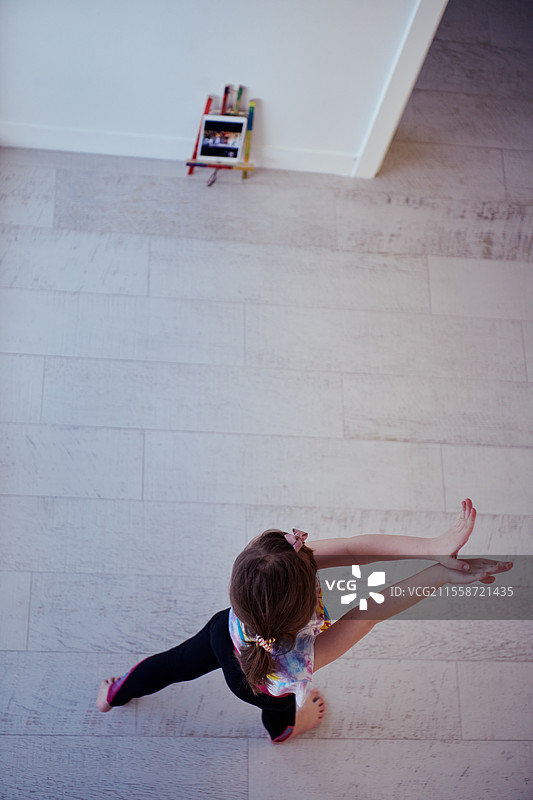 小女孩在家通过平板电脑进行在线培训，正在做现代芭蕾舞练习。现代芭蕾舞学校的在线教育概念课程。在冠状病毒隔离期间保持社交距离，俯视图。图片素材