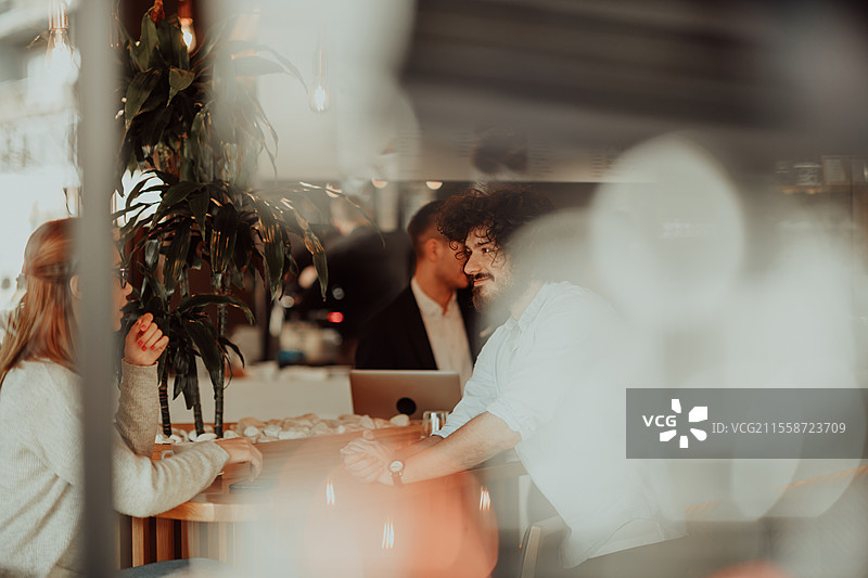 一位戴眼镜的女性和几位有非洲卷发的男性坐在咖啡馆里讨论商业项目。商业情侣在工作日后坐在咖啡馆里。图片素材