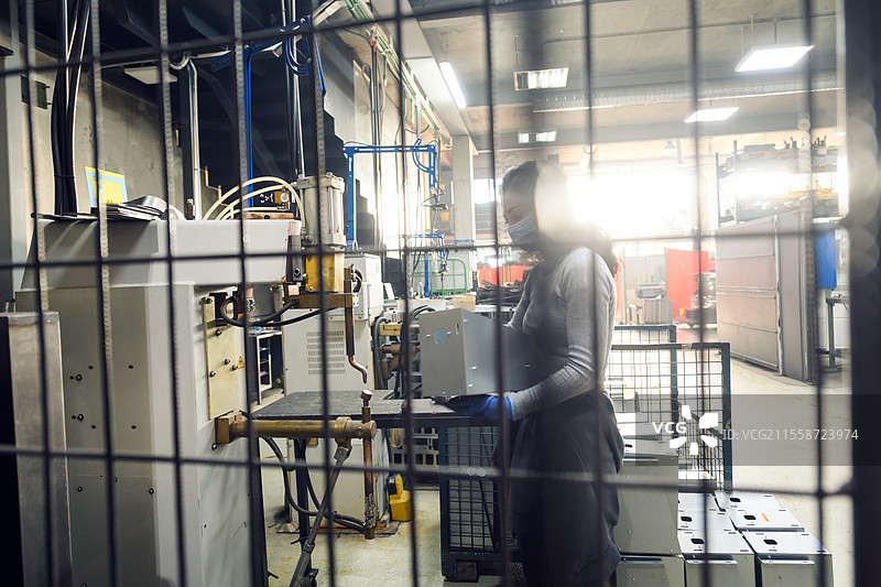 女性在金属行业工作，因新冠疫情在生产新机器时佩戴口罩。高质量照片。图片素材