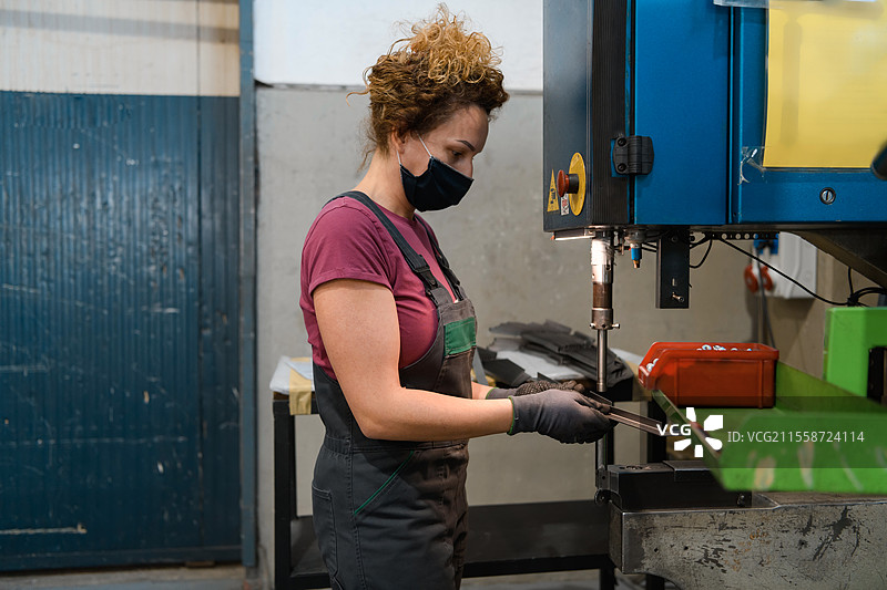 戴着口罩的女性因新冠疫情在现代金属工业中工作并使用电钻。高质量照片。图片素材