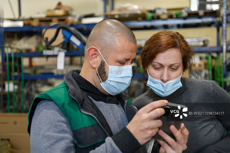 工业工人佩戴口罩以防新冠病毒，在工厂内讨论生产。人们在COVID-19疫情期间工作。高质量照片。图片素材