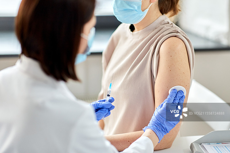 健康、医学和疫情概念 - 女医生或护士戴着防护手套，近距离使用注射器为患者接种疫苗。女医生用注射器为患者接种疫苗。图片素材