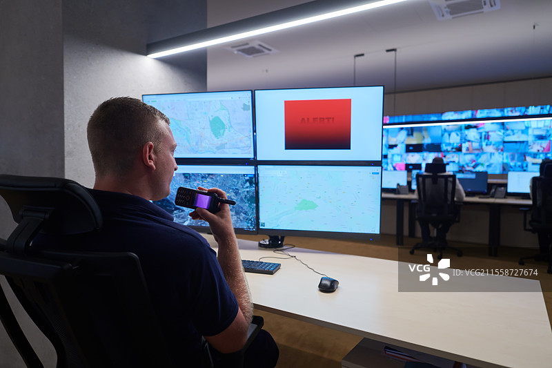 男性安全操作员在数据系统控制室工作，技术操作员在多个显示器的工作站上工作，安全警卫在多个监视器上工作，男性计算机操作员在安全中心进行监控，屏幕上显示警报信号。图片素材