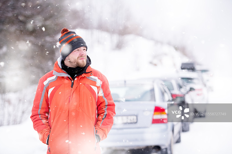冬季的年轻男子肖像，穿着温暖的衣服，享受着雪花飘落的雪天，身处冬季森林中。图片素材