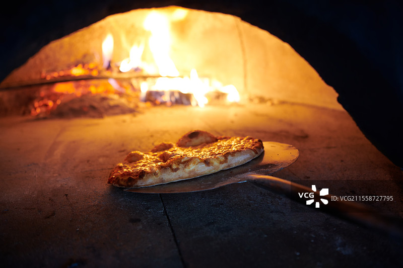 从热炉中取出的乡村披萨。厨师使用特殊的铲子将其取出。这家餐厅有特别的木火烤箱。图片素材
