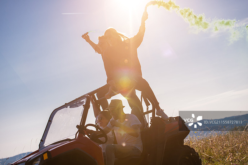 一群年轻快乐兴奋的人在美丽的阳光明媚的日子里，手持五彩缤纷的火把，驾驶越野车在山间大自然中尽情享受乐趣。图片素材