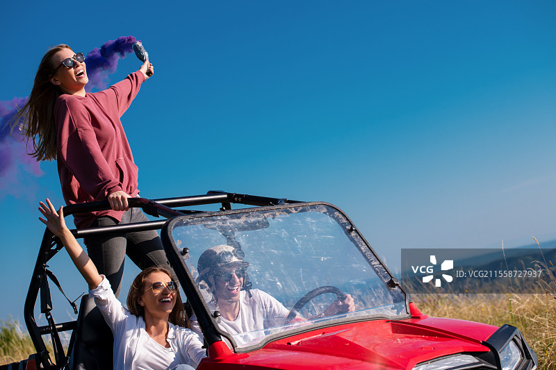 一群年轻快乐兴奋的人在美丽的阳光明媚的日子里，手持五彩缤纷的火把，驾驶越野车在山间大自然中尽情享受乐趣。图片素材