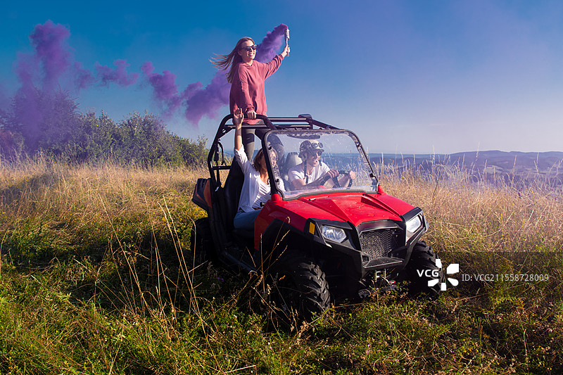 一群年轻快乐兴奋的人在美丽的阳光明媚的日子里，手持五彩缤纷的火把，驾驶越野车在山间大自然中尽情享受乐趣。图片素材