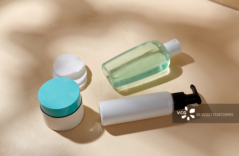 美容、化妆品和物品概念 - 米色表面上有身体乳、乳液、保湿霜和棉垫，伴有阴影。身体乳、乳液、保湿霜和棉垫。图片素材