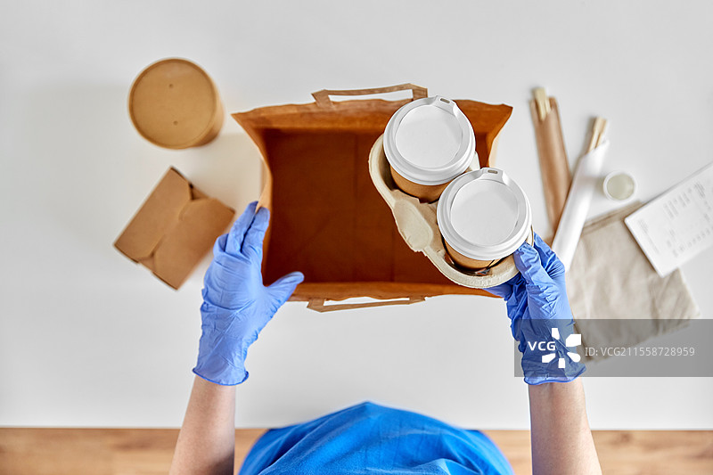 健康保护、安全和疫情概念 - 戴手套的送货员正在将食品和饮料装入纸袋中。图片素材