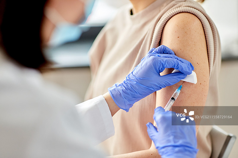 健康、医学和疫情概念 - 女医生或护士戴着防护手套，使用注射器为患者接种疫苗的特写。女医生用注射器为患者接种疫苗。图片素材