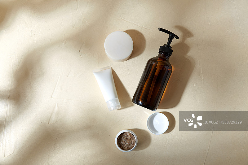 美容、化妆品和物品概念 - 浴 gel、香皂、身体磨砂膏和保湿霜的瓶子放在米色表面上，伴有阴影。浴 gel、香皂、保湿霜和身体磨砂膏。图片素材