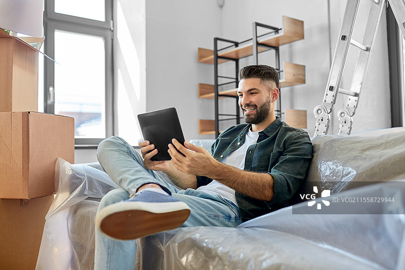搬家、人物与房地产概念 - 开心微笑的男子手持平板电脑和箱子在新家。男子与平板电脑和箱子一起搬入新家。图片素材