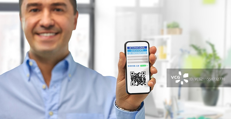 科技与医疗保健概念 - 男性在办公室近距离展示智能手机屏幕上的虚拟免疫护照或国际疫苗接种证明。男性手持智能手机上的虚拟免疫护照。图片素材
