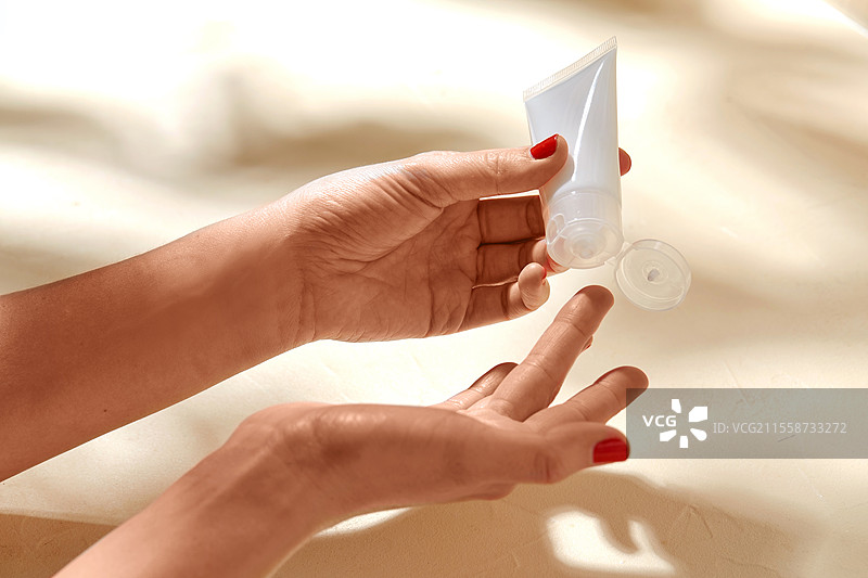 美容产品、化妆品和人群概念 - 女性手部在米色背景下用乳霜管涂抹保湿霜到手指上。女性手部在涂抹保湿霜到皮肤上。图片素材