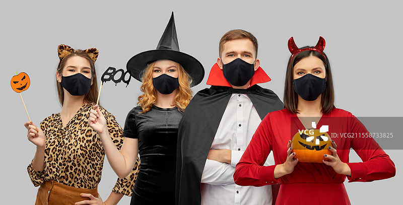 假期、健康和疫情概念 - 朋友们穿着万圣节服装和黑色可重复使用口罩，背景为灰色。朋友们穿着万圣节服装和黑色口罩。图片素材