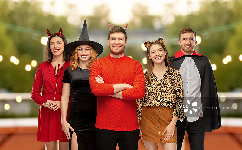 友谊、假期和人们的概念 - 一群快乐微笑的朋友穿着吸血鬼、恶魔、女巫和豹子的万圣节服装，背景是屋顶派对。快乐的朋友们在派对上穿着万圣节服装。图片素材