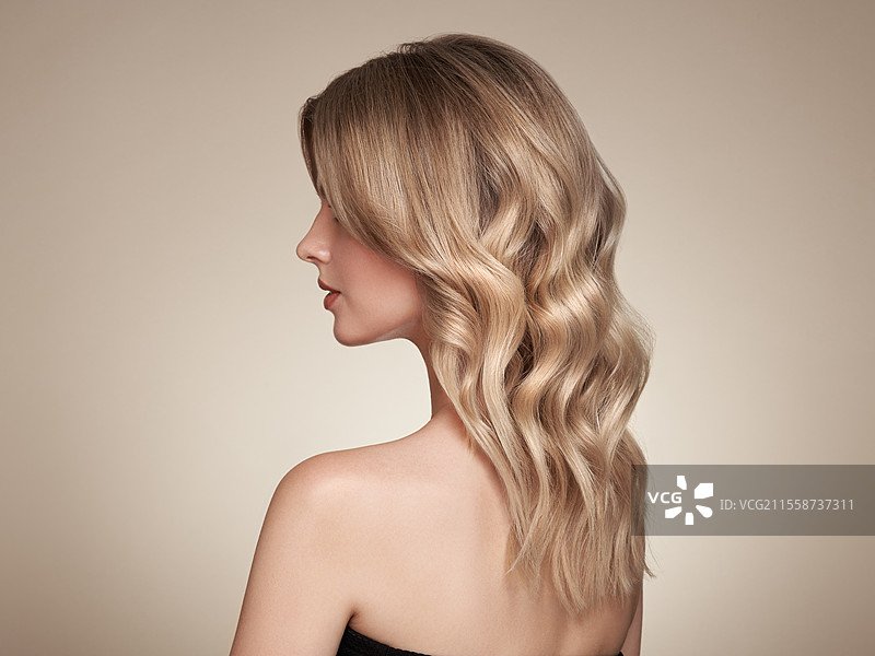 金发女郎，长发卷曲且光泽迷人。美丽的模特女孩，拥有卷发造型。护发和美容产品。图片素材