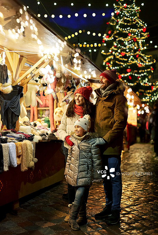 家庭、冬季假期和庆祝概念 - 快乐的母亲、父亲和小女儿在爱沙尼亚塔林市政厅广场的圣诞市场。快乐的家庭在城市的圣诞市场上。图片素材