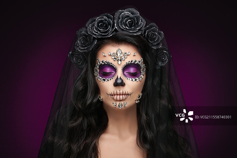 紫色背景下的女性肖像，脸上画着糖骷髅妆。万圣节服装和化妆。卡拉维拉·卡特里娜的肖像。图片素材