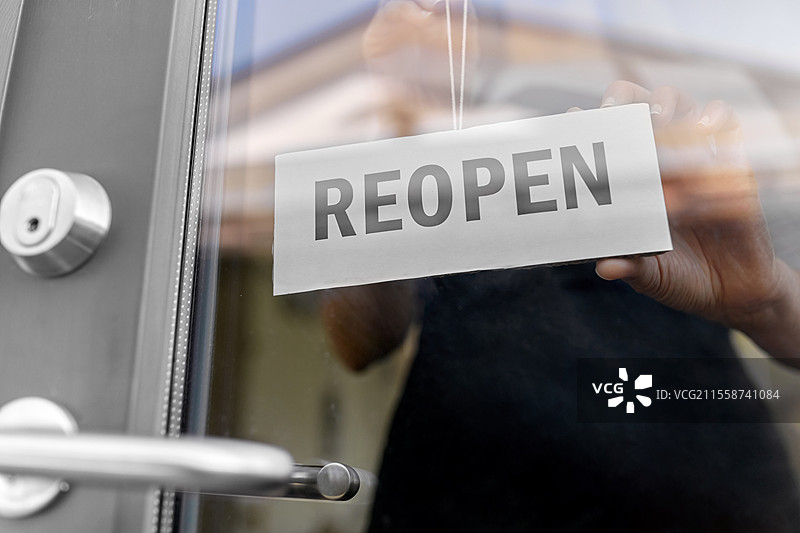 小型企业，重新开业和服务概念 - 特写镜头显示女性在窗户或门玻璃上悬挂重新开业的横幅。特写镜头显示女性在门上悬挂重新开业的横幅。图片素材