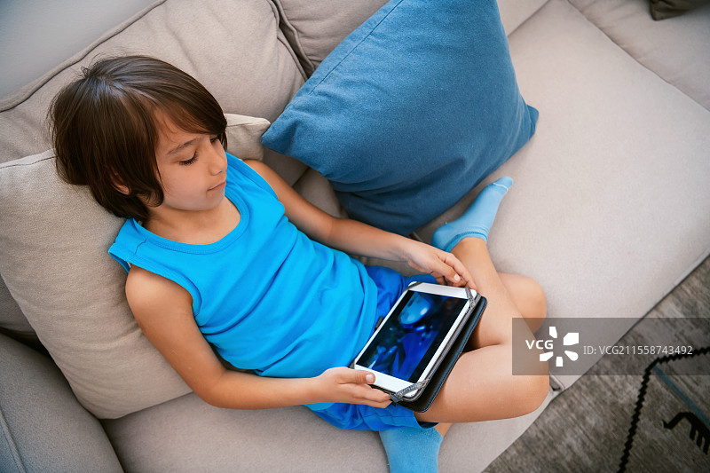 一个阿拉伯男孩坐在沙发上玩平板电脑。高质量照片。图片素材