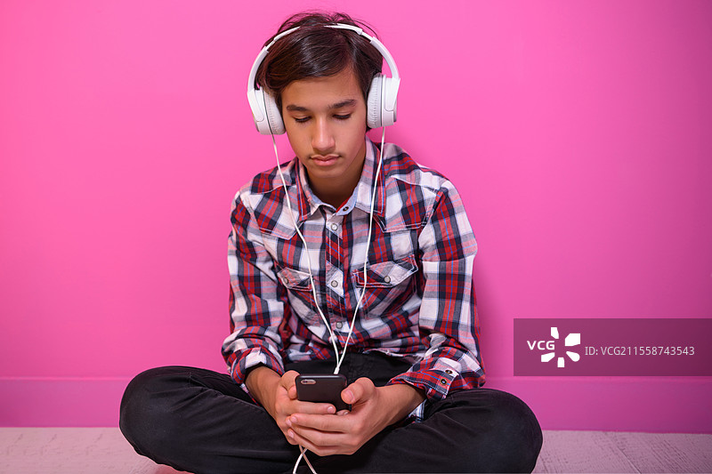 阿拉伯少年戴着耳机听音乐，粉色背景。高质量照片。阿拉伯少年戴着耳机听音乐，粉色背景。图片素材