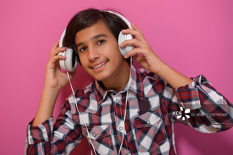阿拉伯少年戴着耳机听音乐，粉色背景。高质量照片。图片素材