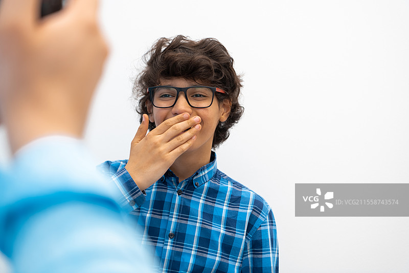 戴着眼镜、穿着休闲校服的阿拉伯少年，头戴帽子，背景为白色空白，展现出聪明的形象。高质量照片。图片素材