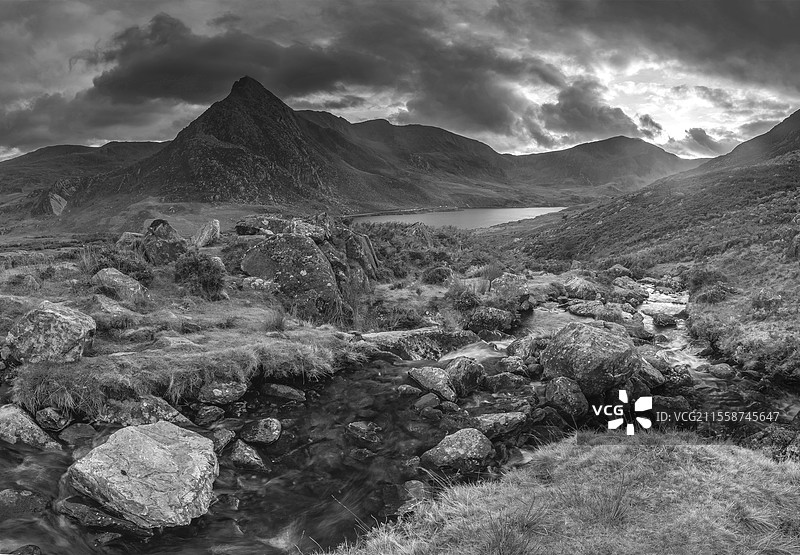 黑白史诗般戏剧性的秋季日落风景图，展示了斯诺多尼亚国家公园的奥格温湖和特里凡山，前景有溪流和岩石。图片素材