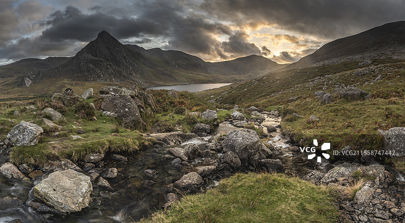 史诗般的戏剧性秋季日落风景，展现了斯诺多尼亚国家公园的奥格温湖和特里凡山，前景有溪流和岩石。图片素材