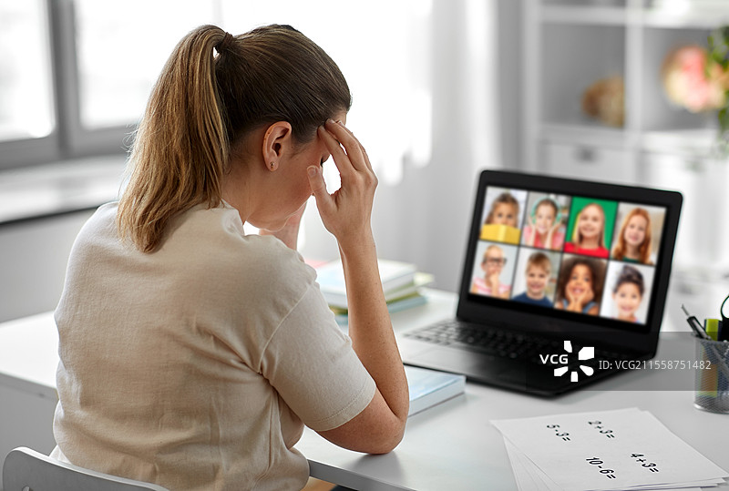 远程教育、远程工作和健康概念 - 疲惫的女教师在家中办公室通过笔记本电脑屏幕与孩子们上课，感到头痛。疲惫的教师在家中进行在线课堂。图片素材