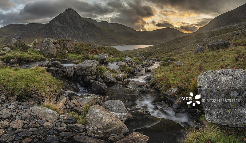 史诗般的戏剧性秋季日落风景，展示了斯诺多尼亚国家公园的奥格温湖和特里凡山，前景有溪流和岩石。图片素材