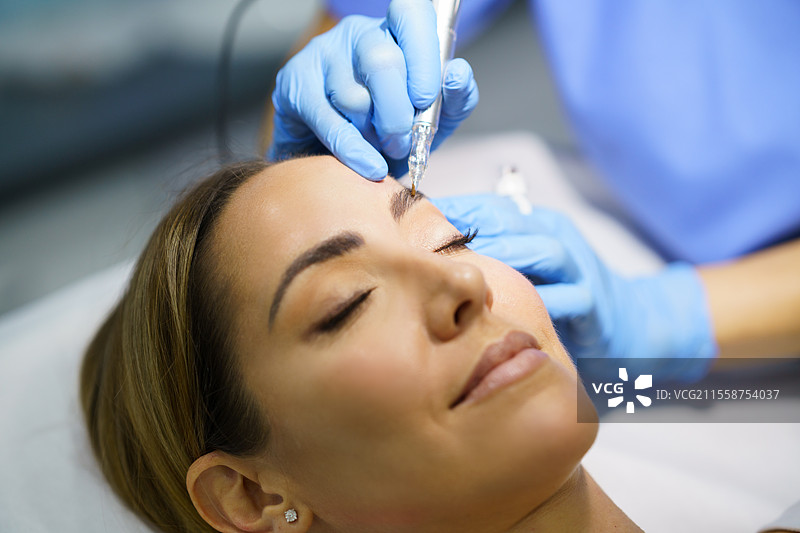 美容院中美丽女性的眉毛永久化妆。美容师正在进行眉毛纹身的特写。微色素沉着治疗。图片素材