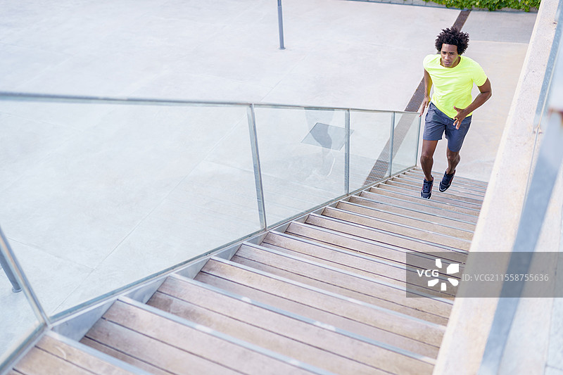 夏季城市中，一位健壮的非裔美国男性跑者在楼梯上进行有氧训练。黑人运动员在城市中向上跑。图片素材