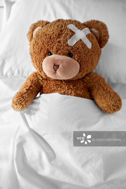 医学、医疗保健和儿童概念 - 受伤的泰迪熊玩具，头上贴着医疗贴，躺在床上。泰迪熊头上贴着医疗贴，躺在床上。图片素材