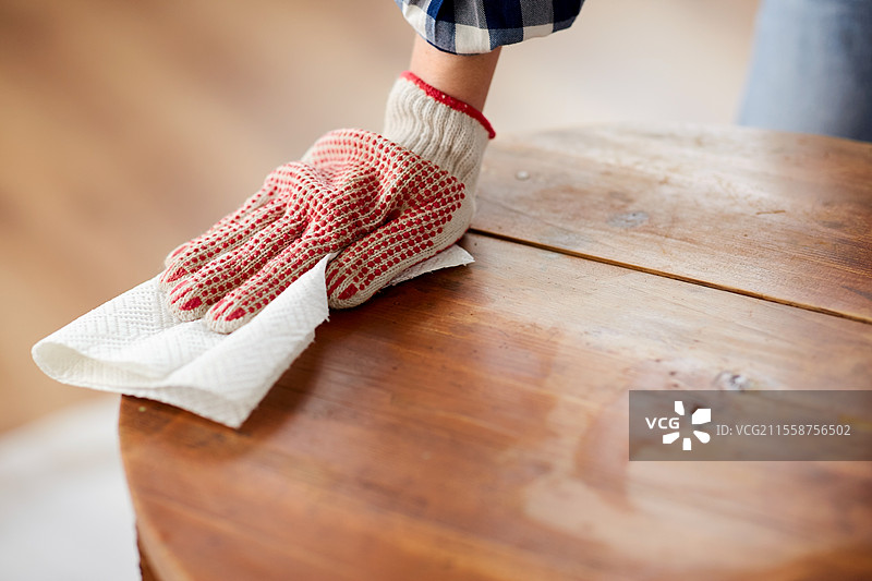 家具翻新，DIY和家居改善概念 - 特写镜头显示女性用纸巾清洁或去油旧圆形木桌表面。女性用纸巾清洁旧桌面。图片素材