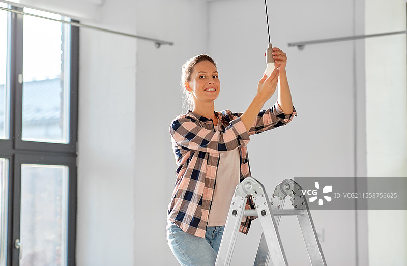 移动、电力和维修概念 - 女人在新家更换灯泡。女人在新家更换灯泡。图片素材