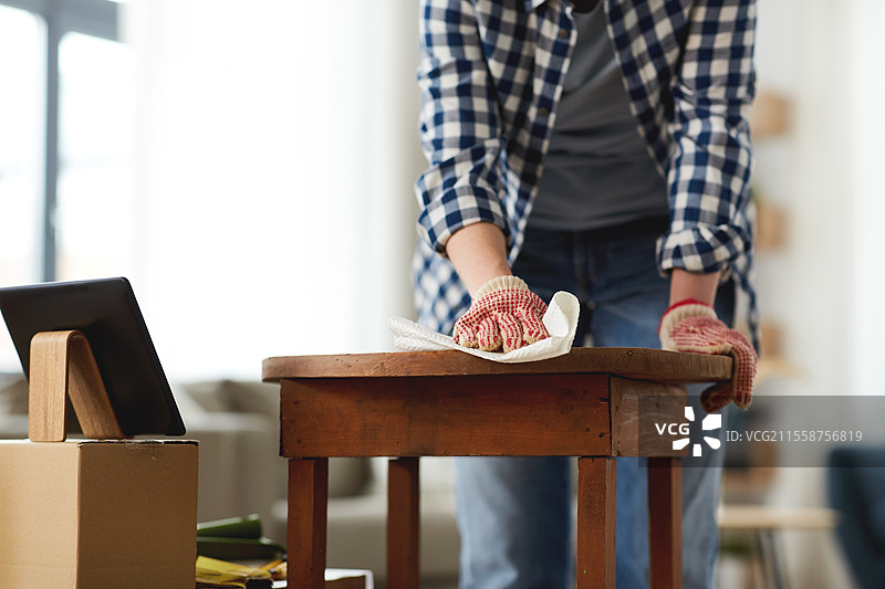 家具翻新、DIY和家居改善概念 - 特写镜头显示一位女性使用平板电脑清洁或去油旧圆形木桌表面，女性正在用纸巾清洁旧桌面。图片素材