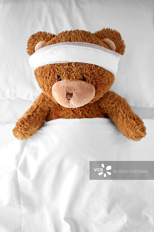 医学、医疗和儿童概念 - 受伤的泰迪熊玩具，头部包扎着，躺在床上。受伤的泰迪熊玩具，头部包扎着，躺在床上。图片素材